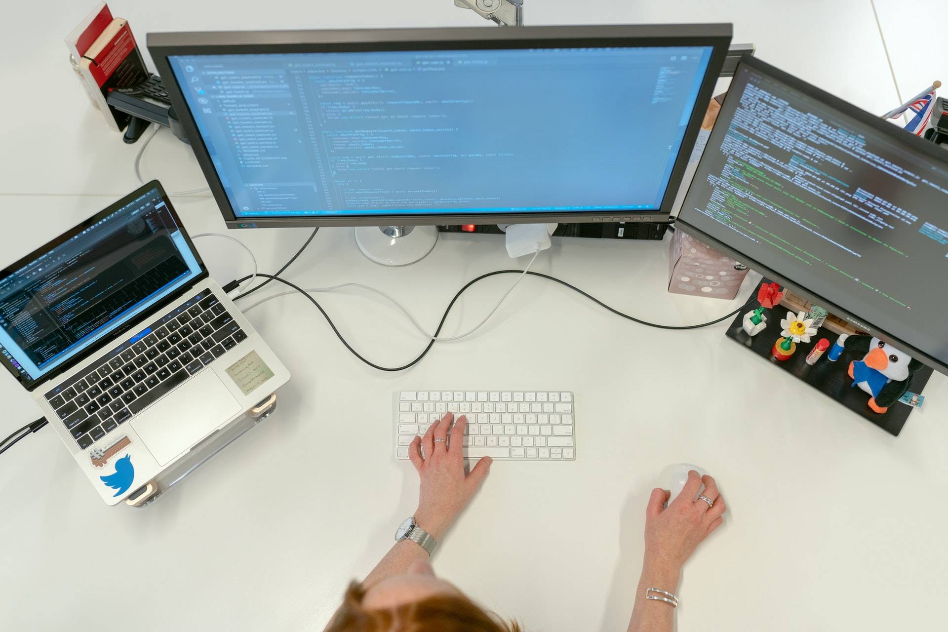 overhead view of person working across three pc/laptop screens on a white desk